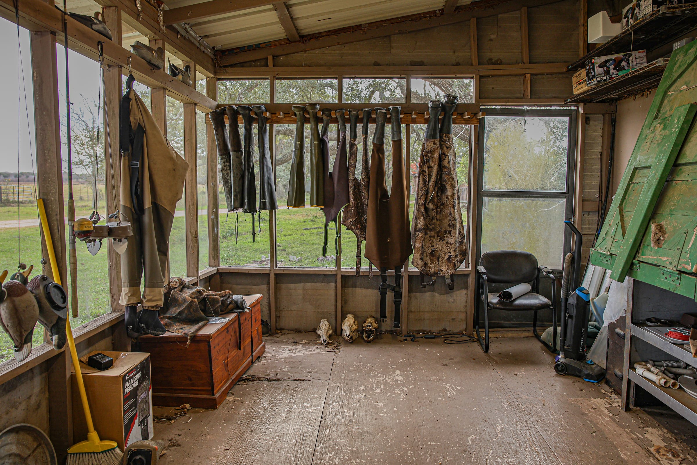 Room with wooden walls, windows looking out on grassland, waders and gear hanging
