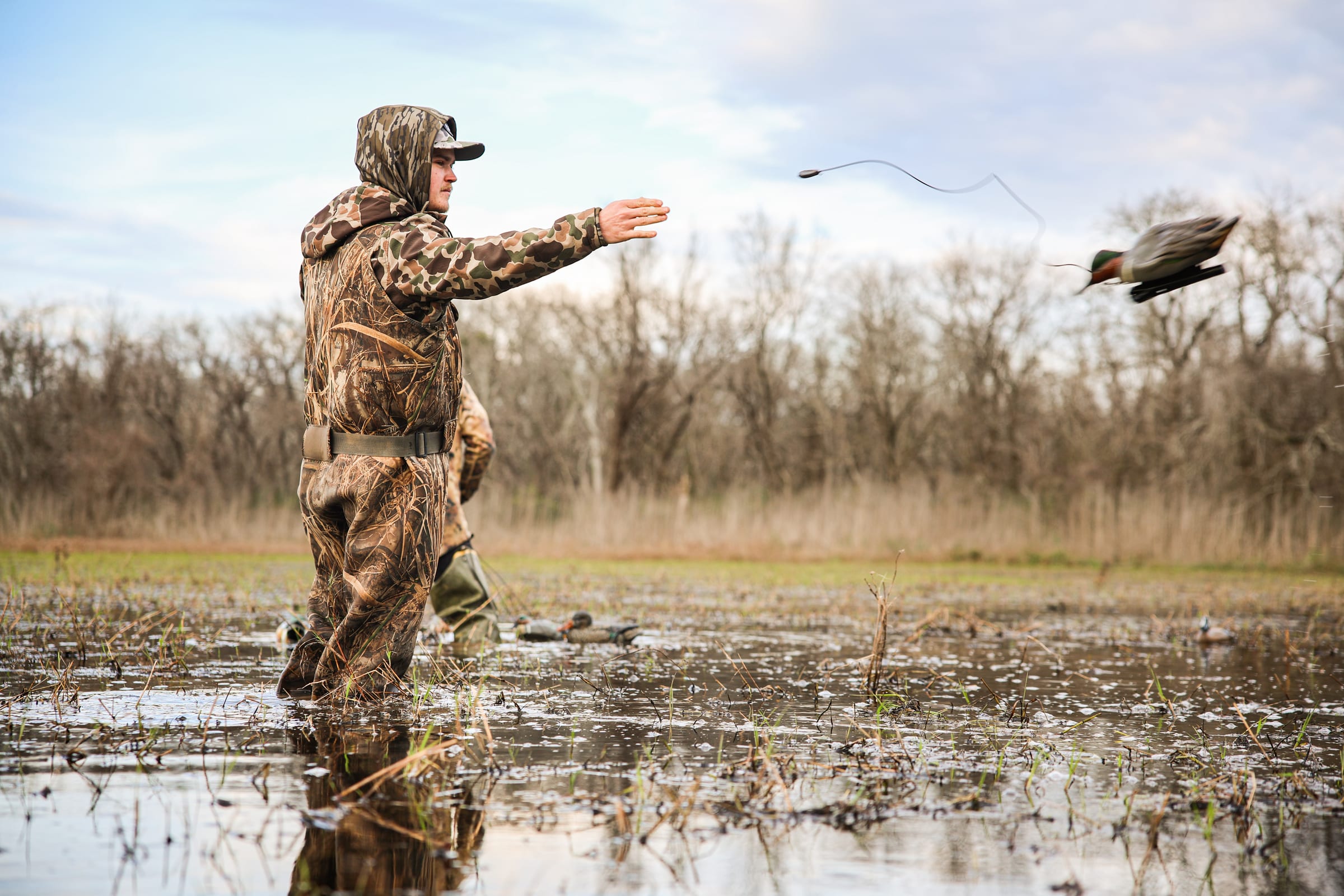 Hunter in camouflage and waders tossing a duck decoy over a flooded field